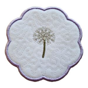 Embroidered candle coaster with a scalloped edge, featuring a delicate dandelion design on a white background with a soft purple border.