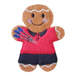 A felt darts player gingerbread character wearing a red shirt and dark trousers, smiling and holding three small blue darts.