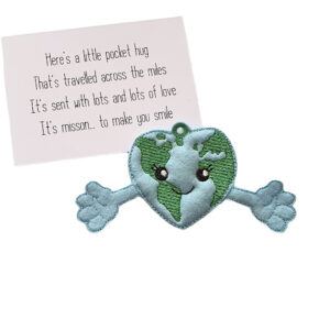 Embroidered Earth heart pocket hug charm made from soft felt, featuring a smiling face and outstretched arms. Displayed with a keepsake card that reads: ‘Here’s a little pocket hug that’s travelled across the miles. It’s sent with lots and lots of love. Its mission... to make you smile.’
