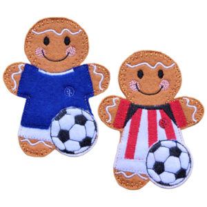 Two felt gingerbread footballer characters, one wearing a blue shirt and white shorts and the other wearing a red and white striped shirt with white shorts. Each character is smiling and standing with a black and white football in front of them.