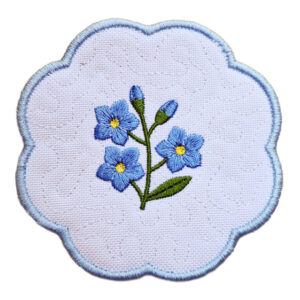 Embroidered Forget Me Not candle coaster with scalloped edge, featuring blue flowers symbolising love and remembrance, green leaves, and light blue border.