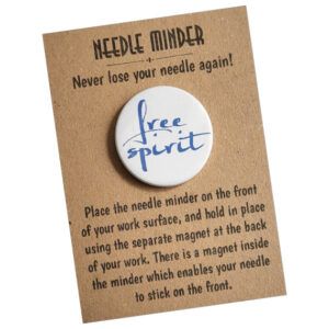 Free Spirit Needle Minder with blue script text on a round white 38mm magnet, designed to hold needles securely for cross stitch or embroidery, displayed on kraft card packaging with printed instructions.