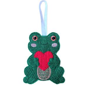 Smiling felt frog holding a heart, machine embroidered with a knit stitch pattern and hanging from a ribbon on a white background