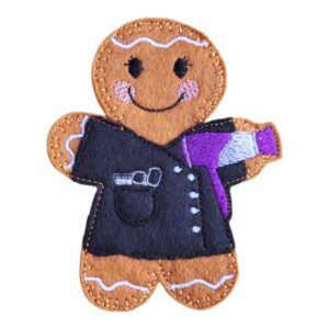 Felt gingerbread character wearing a black hairdresser’s tunic and holding a purple and silver embroidered hairdryer, with a smiling face and stitched decorative icing details.