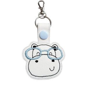 Happy Hippo with Glasses Keyring featuring an embroidered hippo face wearing light blue glasses on white faux leather, with a matching blue snap fastener and metal keyring clasp.