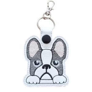 An embroidered keyring shaped like a cute cartoon French Bulldog with large ears, round eyes, and a small nose. The dog has black and white markings, and the keyring includes a silver ring and clasp at the top for attaching to keys or bags.