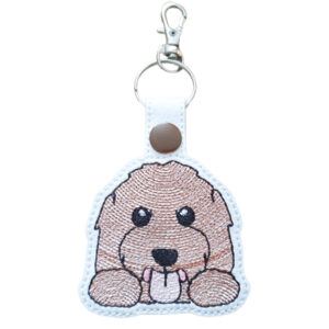 Kawaii Labradoodle Keyring – a cute embroidered dog charm made from white faux leather featuring a smiling Labradoodle with a fluffy face, black nose, and pink tongue, attached to a keyring with a brown snap and lobster clasp.