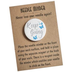 Round white Keep Going Needle Minder with grey script text ‘Keep Going’ and turquoise butterfly accents, 38mm magnetic accessory for cross stitch and embroidery, displayed on kraft card with instructions
