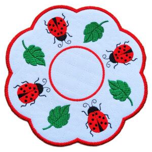 A round decorative candle mat with a scalloped edge, featuring embroidered red ladybirds and green leaves on a white background with a red border.