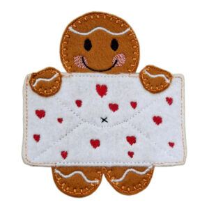 A handmade felt gingerbread character holding a white envelope decorated with small red embroidered hearts and a stitched ‘x’. The cute design features pink blushing cheeks, icing-like embroidery details, and neat stitching, creating a sweet and thoughtful gift or decoration.