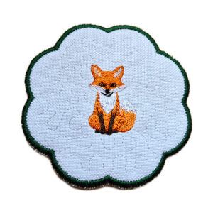 Embroidered woodland fox candle coaster with scalloped edge, dark green border, and central fox design on a soft textured white background
