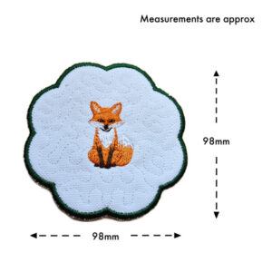 Embroidered woodland fox candle coaster with scalloped edge and dark green border, shown with approximate measurements of 98mm by 98mm