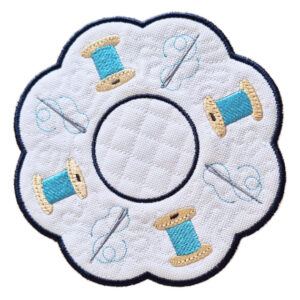 Embroidered needle and thread candle mat with scalloped edge, featuring spools of thread and needle details on a white background, with a central circular space for a candle.