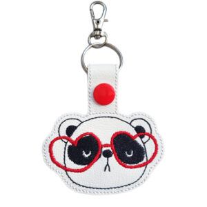 Panda with Heart-Shaped Glasses Keyring featuring an embroidered panda face wearing red heart-shaped glasses on white faux leather, with silver clasp and snap button.