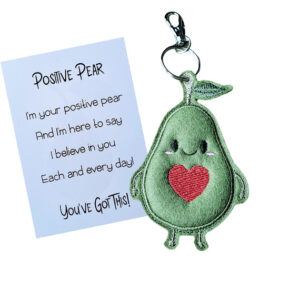Positive Pear Pocket Pal keyring – a cute green pear with a smiling face and a red heart, attached to a silver keyring, shown next to a keepsake card with an encouraging message: ‘I'm your positive pear and I'm here to say I believe in you each and every day. You've got this!’