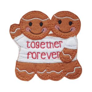 Two smiling felt gingerbread figures cuddled together in a single oversized T-shirt, embroidered with the words ‘Together Forever.’ A handmade decoration symbolising love, warmth, and togetherness, measuring about 4 inches tall.
