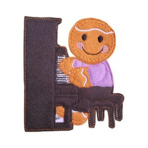 A felt gingerbread character is seated at a piano, smiling with rosy cheeks. The piano and stool are stitched in dark felt, while the gingerbread character wears a light purple top. The piece is detailed with embroidered icing-style lines and soft fabric textures.