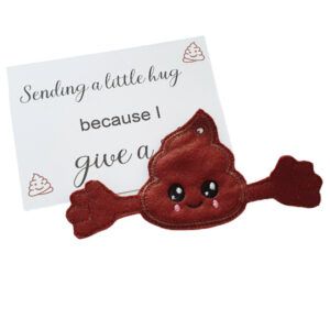 Embroidered poop-shaped pocket hug charm with a smiling face and outstretched arms, made from soft brown felt. Displayed with a keepsake card that reads: ‘Sending a little hug because I give a 💩.’