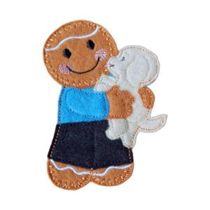 A handmade felt gingerbread character wearing a blue top and black shorts, smiling and holding a small cream-coloured puppy with embroidered details.