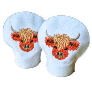 Set of two felt tealight covers in white fabric, each featuring an embroidered Highland cow head on the front, designed to fit over standard LED tealights.