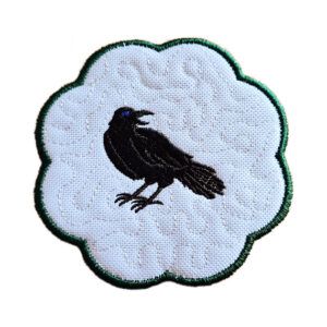 Embroidered raven candle coaster with scalloped edge, featuring a black raven on a textured white background with a subtle stippled pattern.