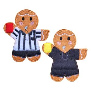 Two felt gingerbread referees holding cards. One wears a black-and-white striped shirt and holds a red card, while the other wears a plain black referee kit and holds a yellow card. Both have whistles and smiling faces.
