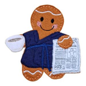 Rise and Shine Gingerbread Character - a handmade felt gingerbread figure wearing a soft dressing gown, smiling while holding a hot cup of tea or coffee in one hand and a stitched newspaper in the other.