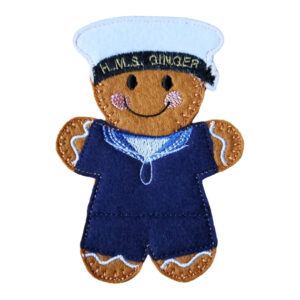 Royal Navy Sailor Gingerbread Character figure dressed in a dark blue uniform with a light blue collar. The character wears a white sailor’s cap embroidered with ‘HMS GINGER’ and features a cheerful smile. A whimsical keepsake tribute to Royal Navy sailors.