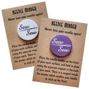 Two round needle minders displayed on kraft card packaging. One has a white background with black script text reading ‘Sew Sew’ and a needle graphic, and the other has a purple background with white script text and the same needle design. Packaging says ‘Needle Minder – Never lose your needle again!’ with instructions.