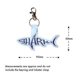 Embroidered shark word art keyring on white faux leather with grey stitching, measuring approximately 95mm wide and 60mm high, excluding the keyring and lobster clasp.