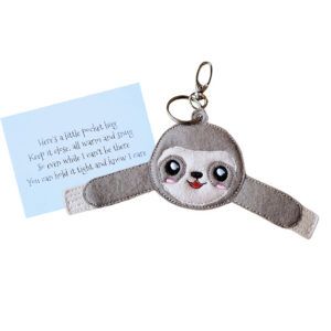 Embroidered sloth pocket hug charm with a smiling face and outstretched arms, made from soft felt. Displayed with a keepsake card that reads: ‘Here’s a little pocket hug. Keep it close, all warm and snug. So even while I can’t be there, you can hold it tight and know I care’.