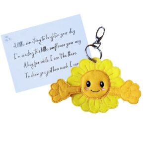A handmade sunflower pocket hug charm made from soft yellow felt with outstretched arms and a smiling embroidered face. Attached to a keyring and clasp, it comes with a keepsake card printed with a heartfelt poem about sending sunshine, love, and hugs from afar.