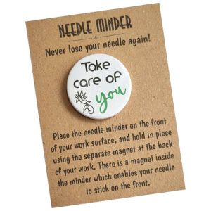 Decorative white needle minder with motivational phrase “Take care of you,” highlighting the word “you” in green, the magnet holds needles securely.
