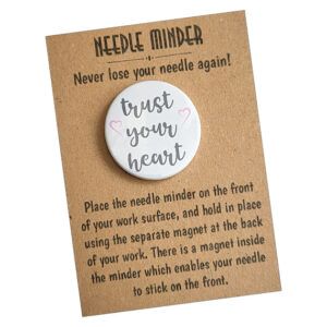 Round needle minder with the phrase “trust your heart” in soft script, displayed on a kraft card with instructions and the heading “Needle Minder – Never lose your needle again!”.