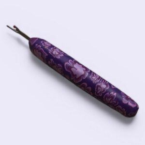 Handmade purple polymer clay stitch picker with floral pattern handle, ergonomic crochet tool designed to help pick stitches and correct knitting or crochet mistakes.