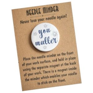 Round white needle minder with the words “you matter” in blue script, surrounded by small starburst designs. Displayed on kraft card backing that explains how to use the needle minder.