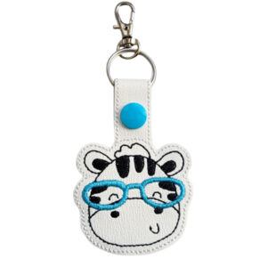 Zebra with Glasses Keyring featuring an embroidered zebra face wearing teal glasses on white faux leather, with a teal snap button and silver clasp.