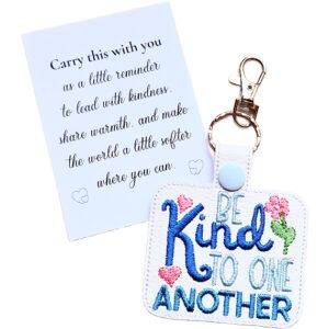 Be Kind to One Another embroidered faux leather keyring with blue text, pink hearts and flowers, gold clasp, and a white keepsake card with a kindness message.