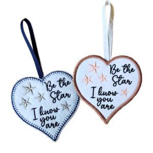 White felt heart hanging decorations with embroidered stars and the message “Be the Star I know you are”, shown with navy blue and rose gold stitched borders and ribbon loops