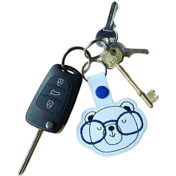 Bear face keyring with blue glasses attached to a set of keys, showing the keyring in everyday use.
