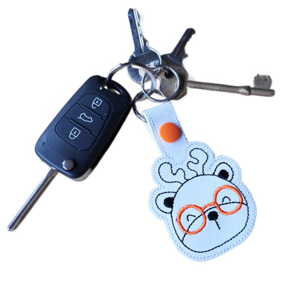 Deer face keyring with orange glasses attached to a set of keys, showing the keyring in everyday use.