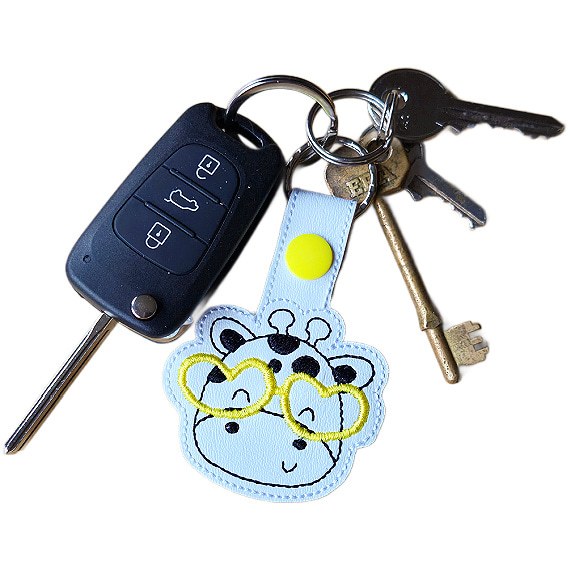 Giraffe face keyring with yellow glasses attached to a set of keys, showing the keyring in everyday use.