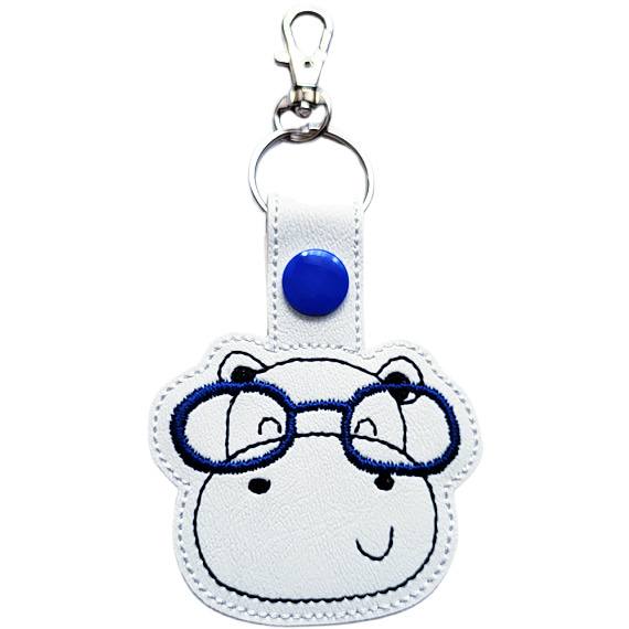Hippo face keyring with navy blue glasses, made from white faux leather with a metal split ring and swivel clasp.
