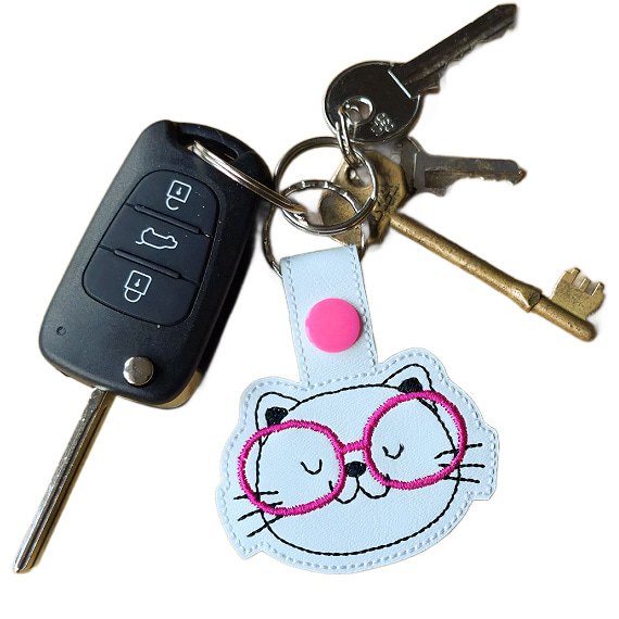 Kitten face keyring with pink glasses attached to a set of keys, showing the keyring in everyday use.