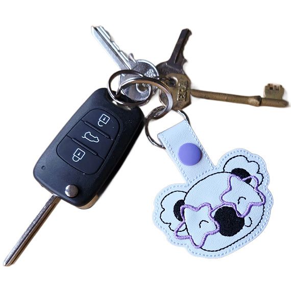 Koala face keyring with purple star glasses attached to a set of keys, showing the keyring in everyday use.
