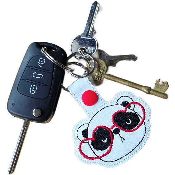 Panda face keyring with red heart glasses attached to a set of keys, showing the keyring in everyday use.
