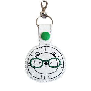 Lion face keyring with green glasses, made from white faux leather with a metal split ring and swivel clasp.
