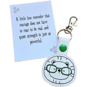 Lion face keyring with green glasses shown with matching keepsake card featuring a courage and quiet strength message.
