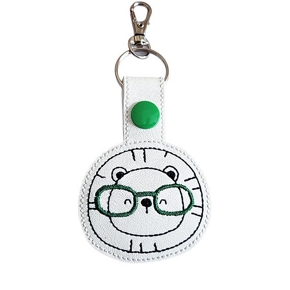 Lion face keyring with green glasses, made from white faux leather with a metal split ring and swivel clasp.