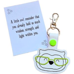 Owl face keyring made from white faux leather with embroidered facial details and bright green glasses, displayed beside a printed keepsake card with the message ‘A little owl reminder that you already hold so much wisdom, strength, and light within you.’